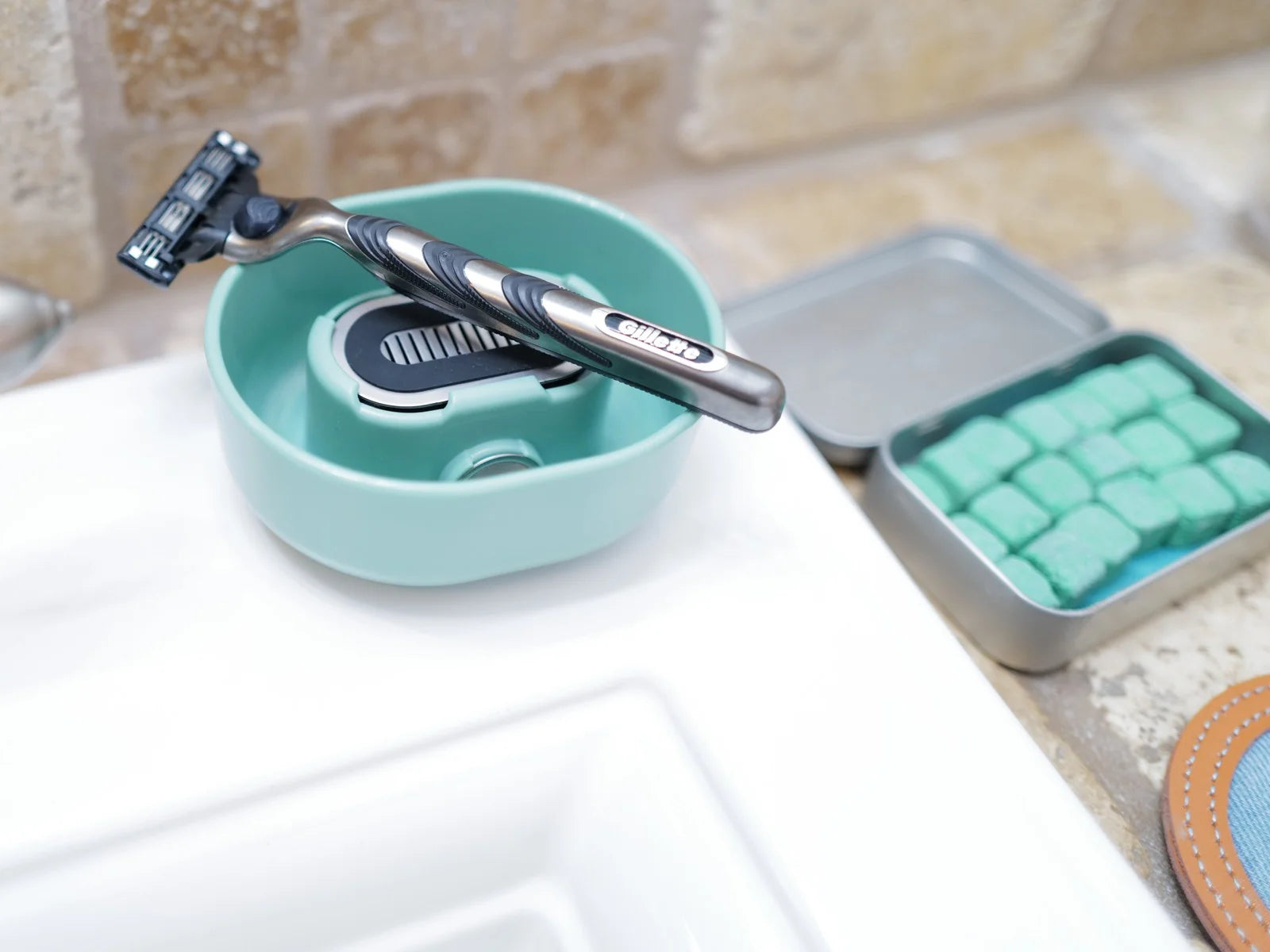 A cartridge razor resting blades up on the Razor Rinser® beside a tin of shave bombs